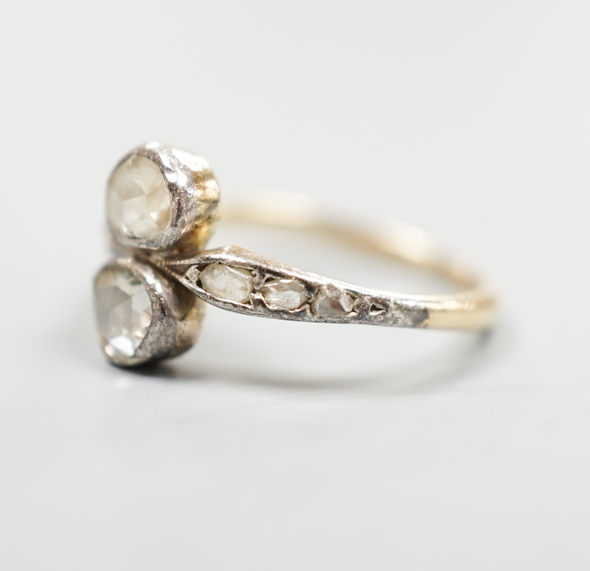 An antique yellow metal and two stone rose cut diamond set crossover ring, with diamond set shoulders, size L, gross weight 2.3 grams.